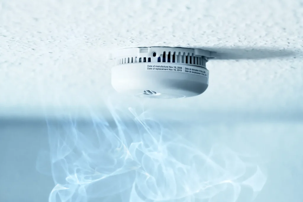 Ceiling-mounted smoke alarm in a rental home with smoke rising toward it