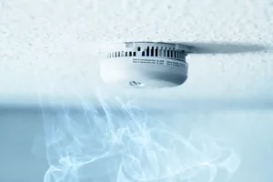 Ceiling-mounted smoke alarm in a rental home with smoke rising toward it