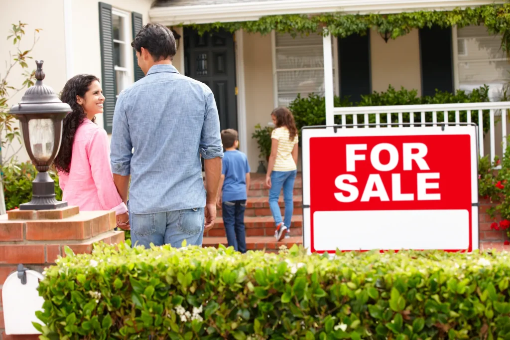 Red For Sale sign in front of a single-family home with a brick walkway and hedges, marking the case for selling your house instead of renting it out