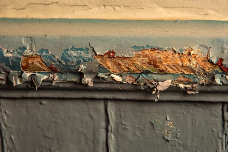 Close-up of peeling, chipped layers of old paint on wood trim, exposing bare wood underneath