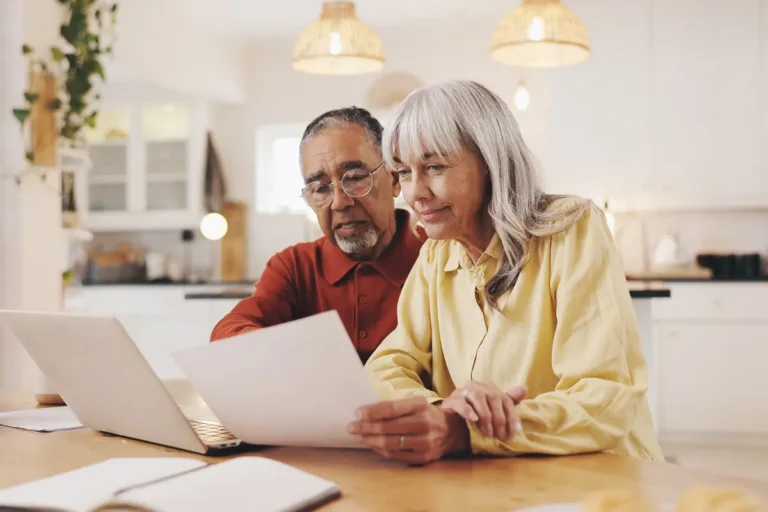 Couple reviewing documents and a laptop at a kitchen table while planning rental property ownership