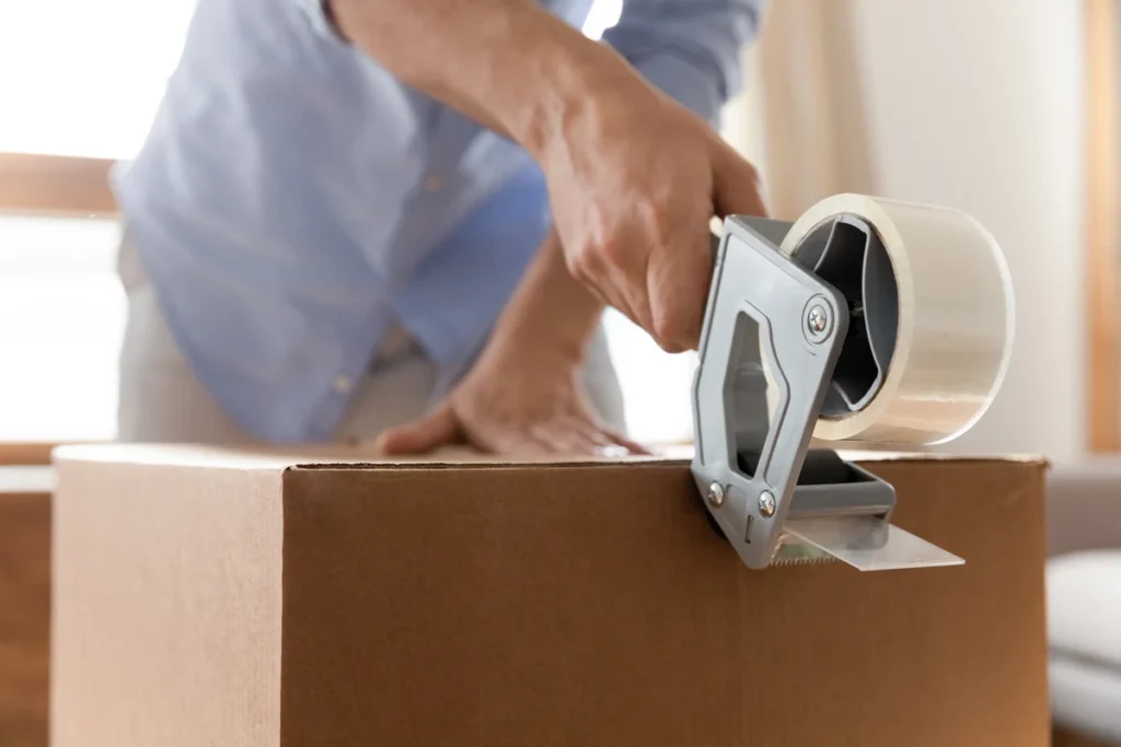 Person sealing a cardboard moving box with packing tape