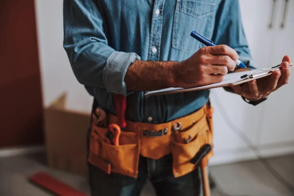 Maintenance worker wearing a tool belt and writing on a clipboard